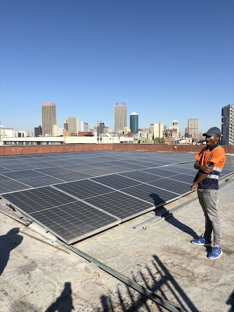 A large rooftop solar array with the Johannesburg skyline behind it