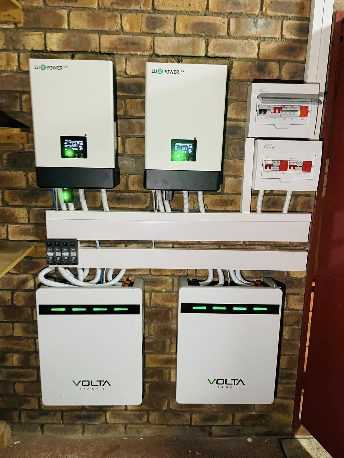 Two hybrid inverters and a pair of lithium batteries installed on a brick wall